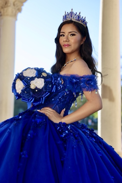 Quinceañera portrait in a royal blue gown with a blue and white bouquet